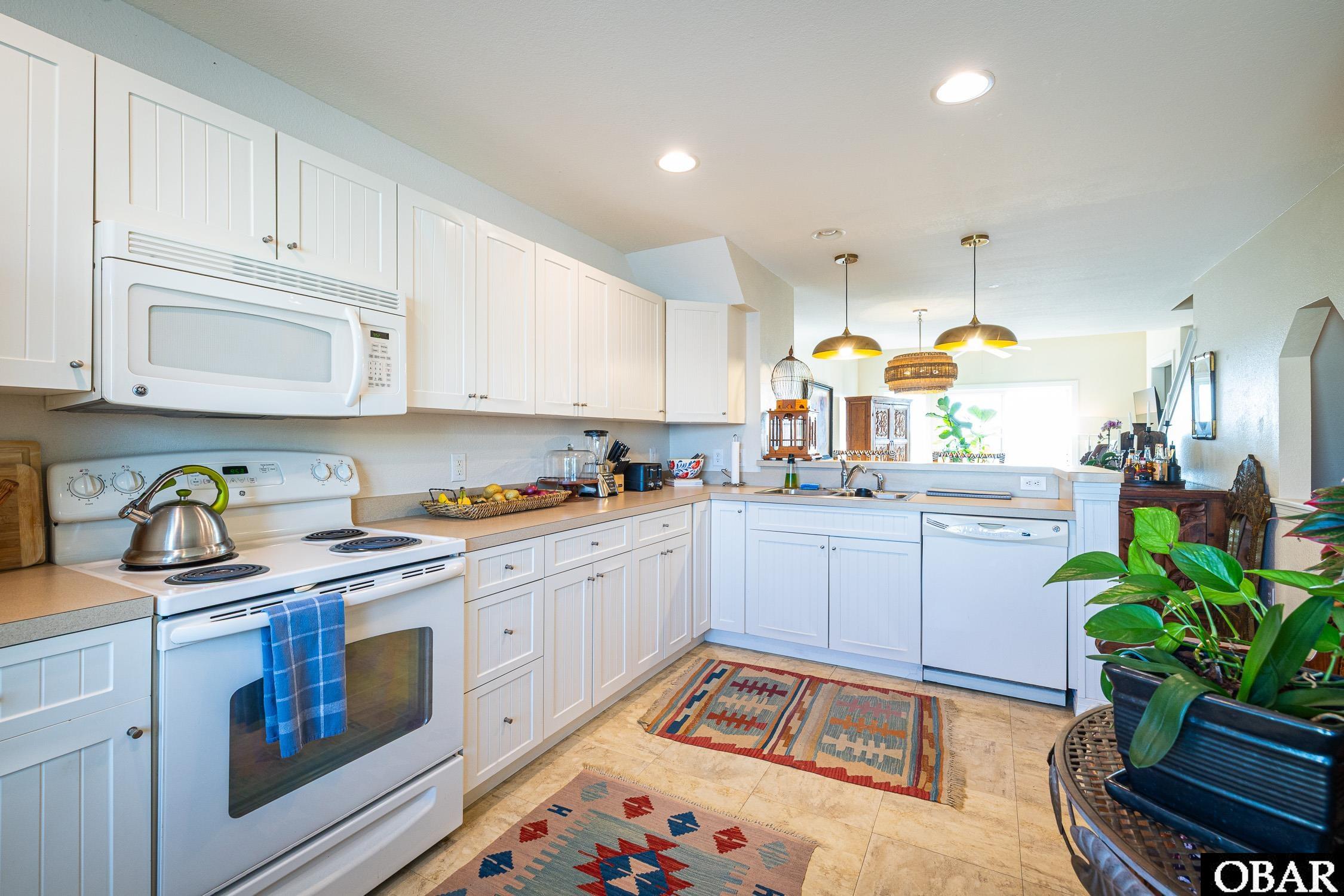 Bright kitchen with white cabinets, electric range, peninsula sink, and colorful patterned rugs.