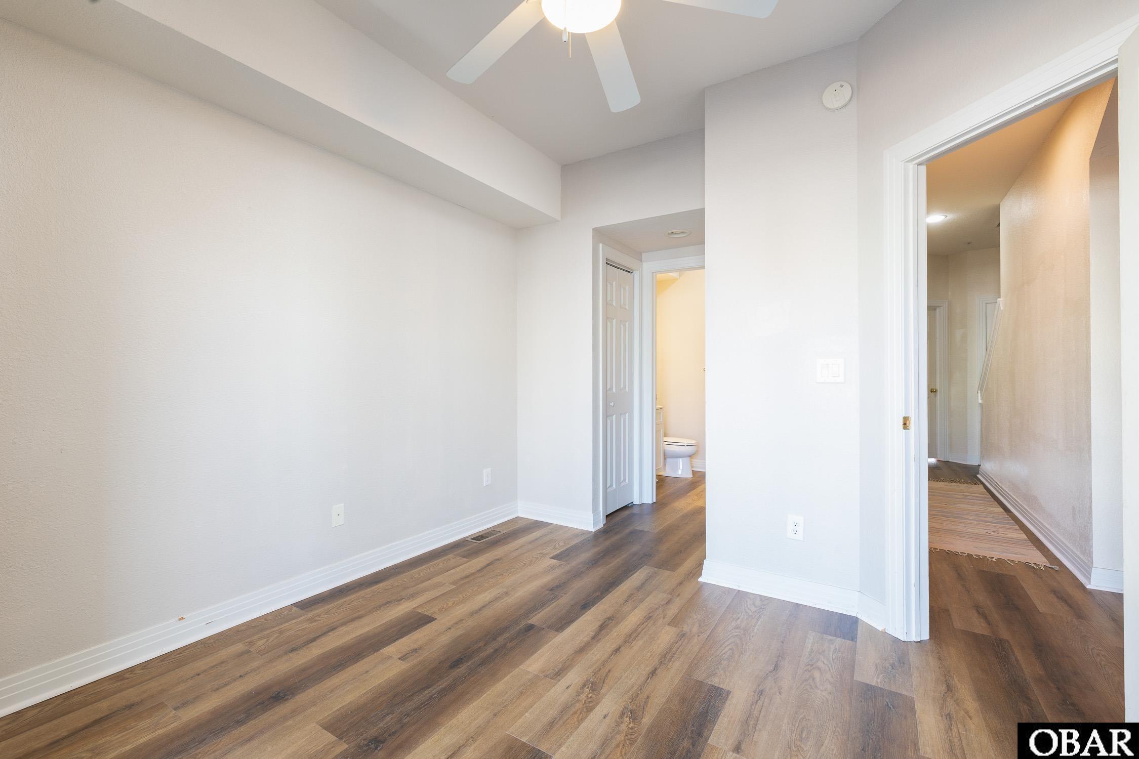 Empty bedroom with wood-look flooring, a ceiling fan, and a bathroom doorway.