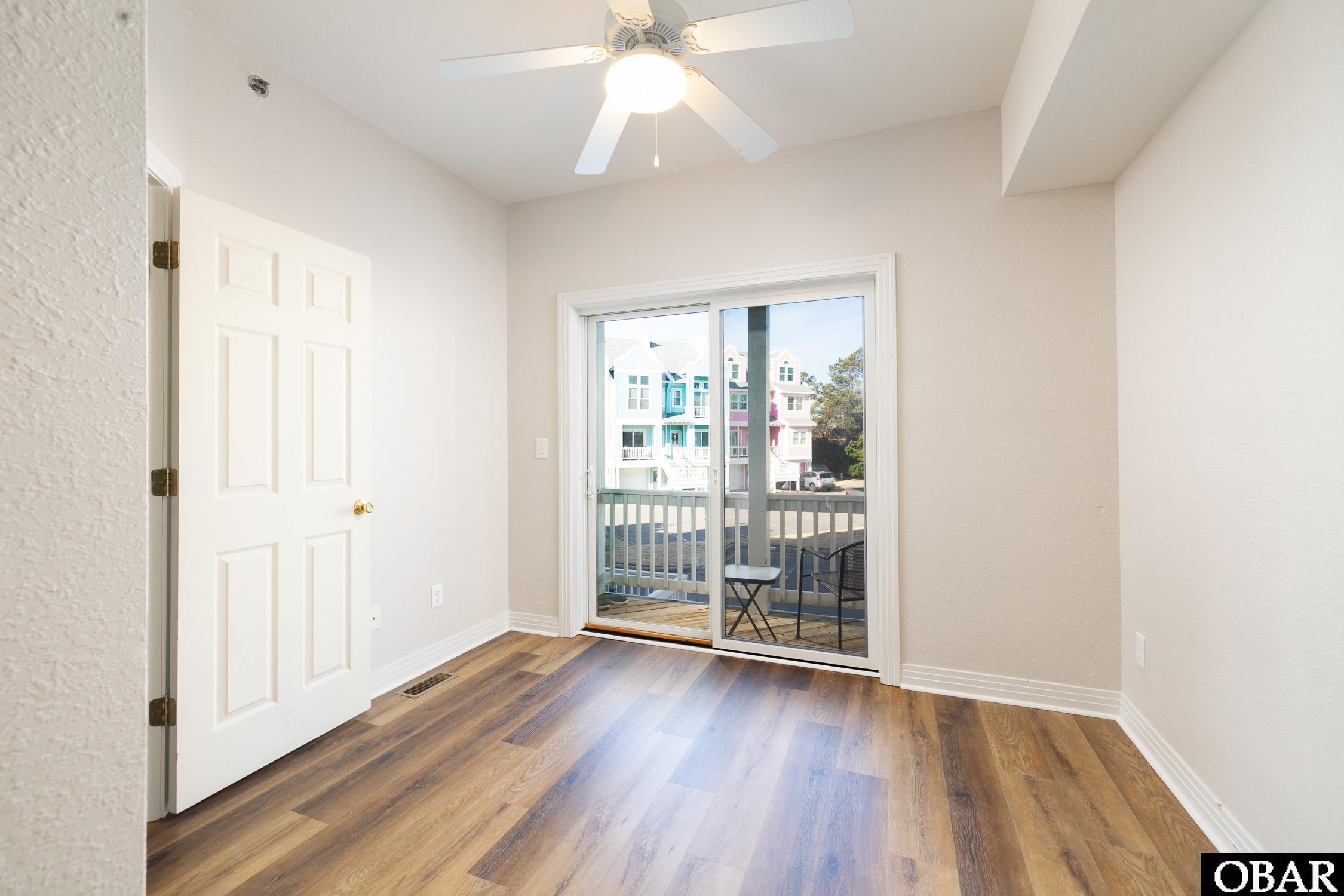 Empty room with wood-look flooring, a ceiling fan, and sliding doors to a balcony.