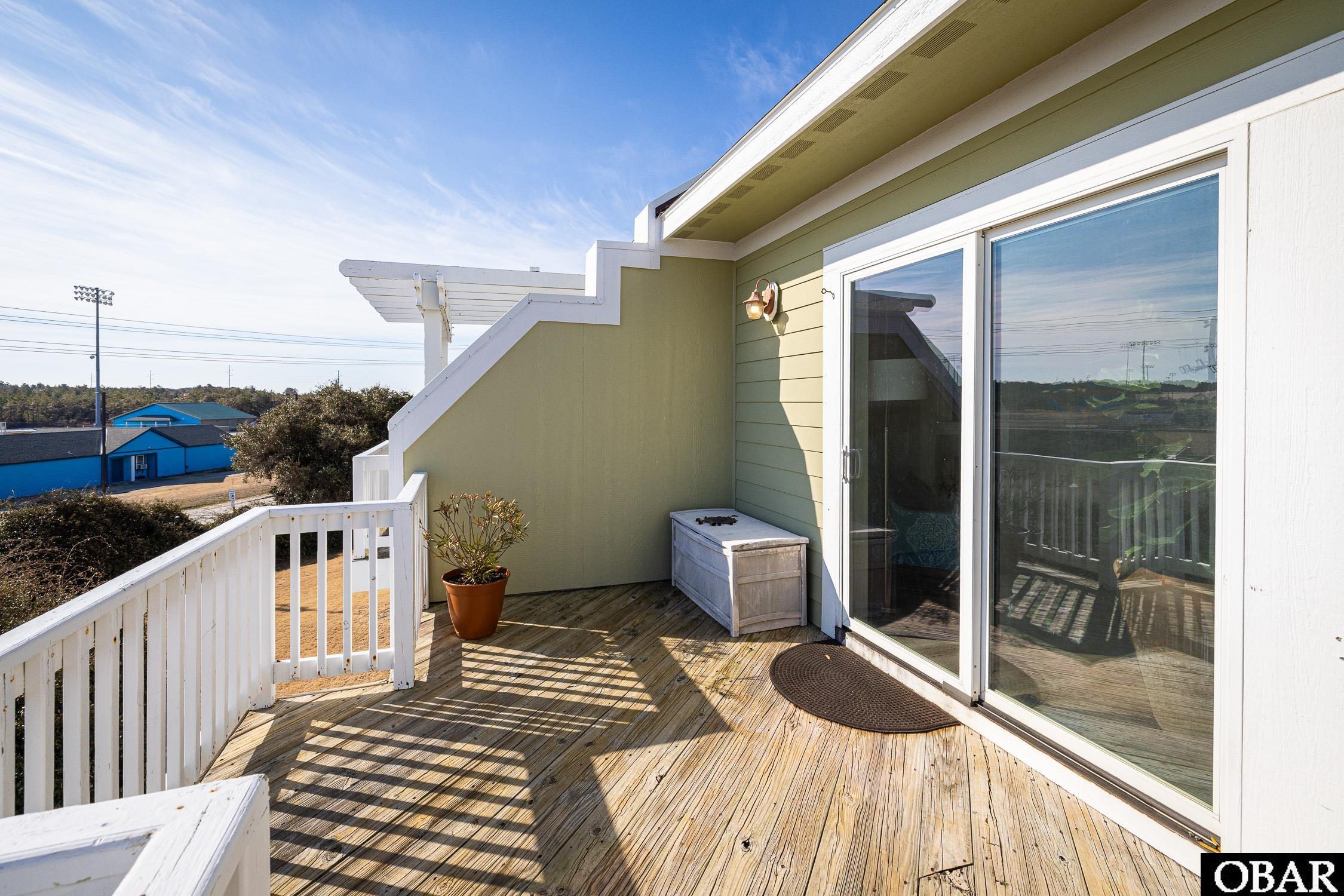 Wooden balcony deck with white railings, sliding glass doors, and a potted plant.