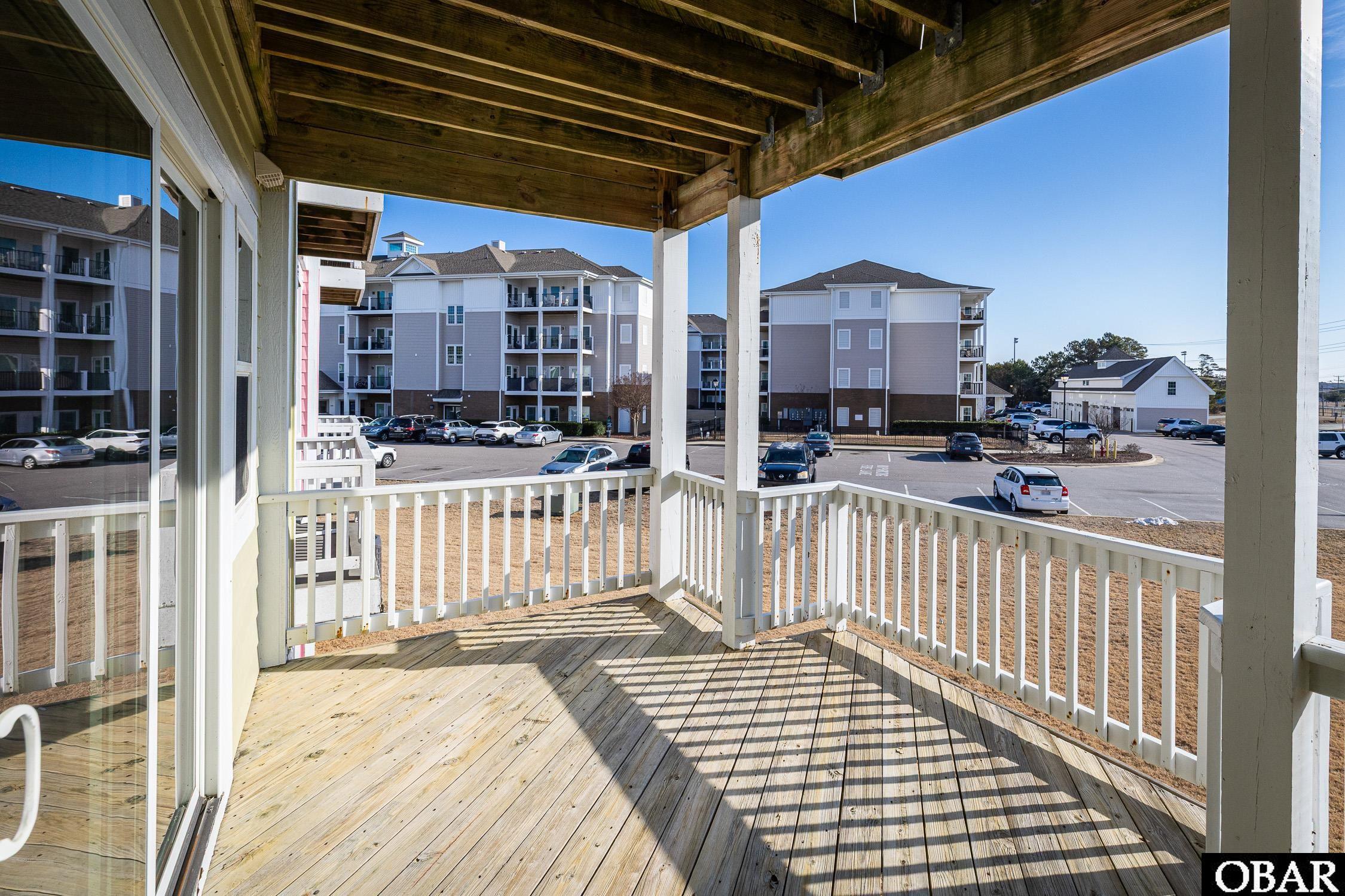 Covered wooden balcony overlooking neighboring condominium buildings and a parking lot.