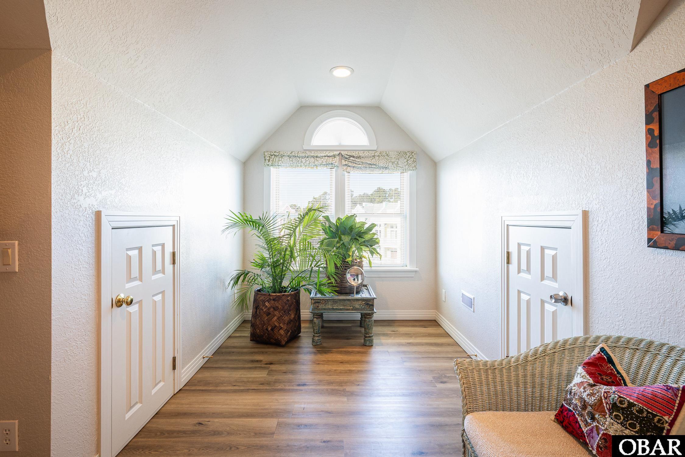 Bright entry hall with a vaulted ceiling, arched window, potted plants, and wicker seating.