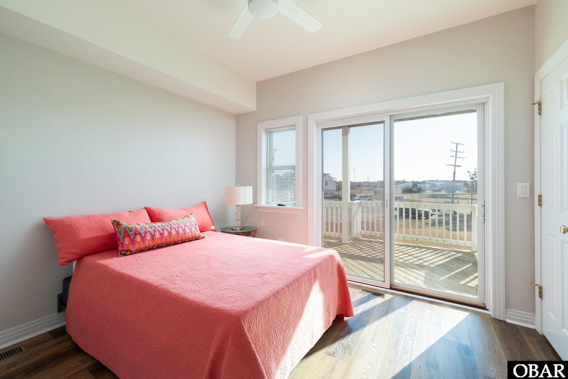 Bedroom with a coral bedspread and sliding glass doors opening onto a deck.