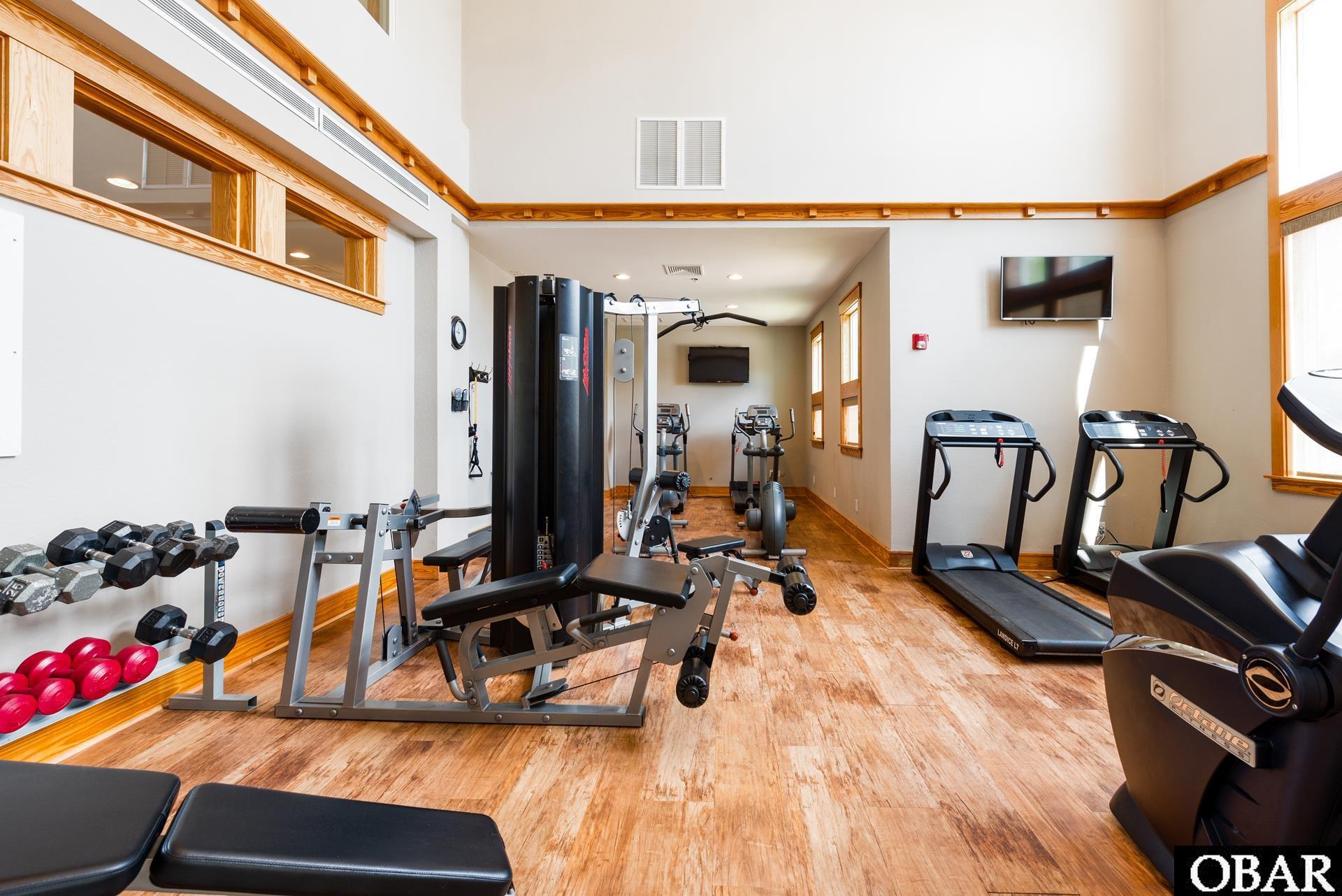 Shared fitness room with treadmills, weight machines, and dumbbells on wood-look flooring.