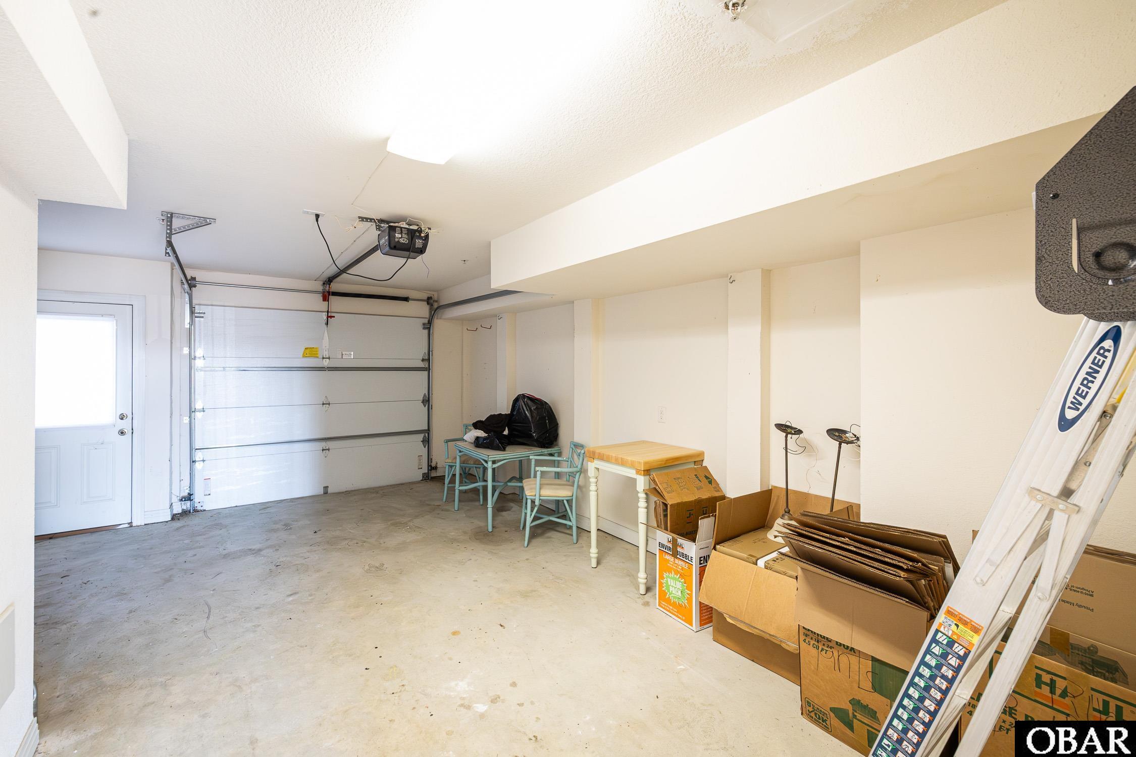 Garage with a closed overhead door, folding table, chairs, storage boxes, and a ladder.