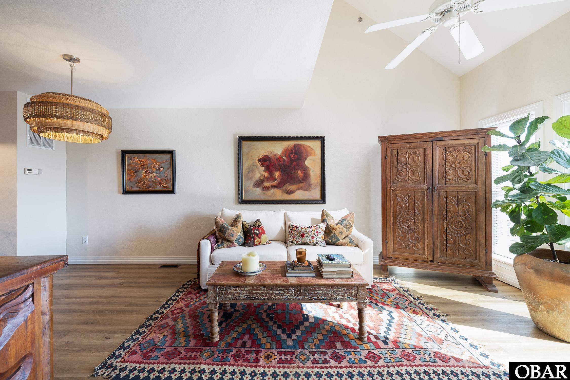 Living room with a white sofa, carved wooden cabinet, patterned rug, and vaulted ceiling.