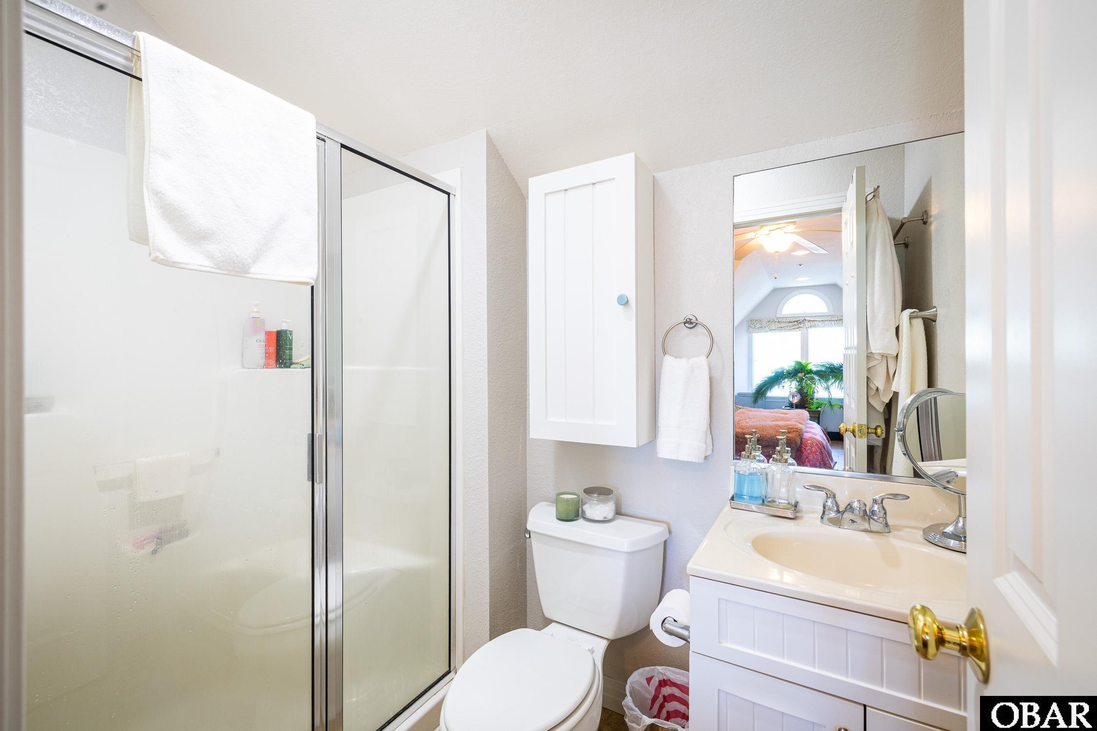 Bathroom with a glass shower, white vanity, and mirror reflecting a bedroom.