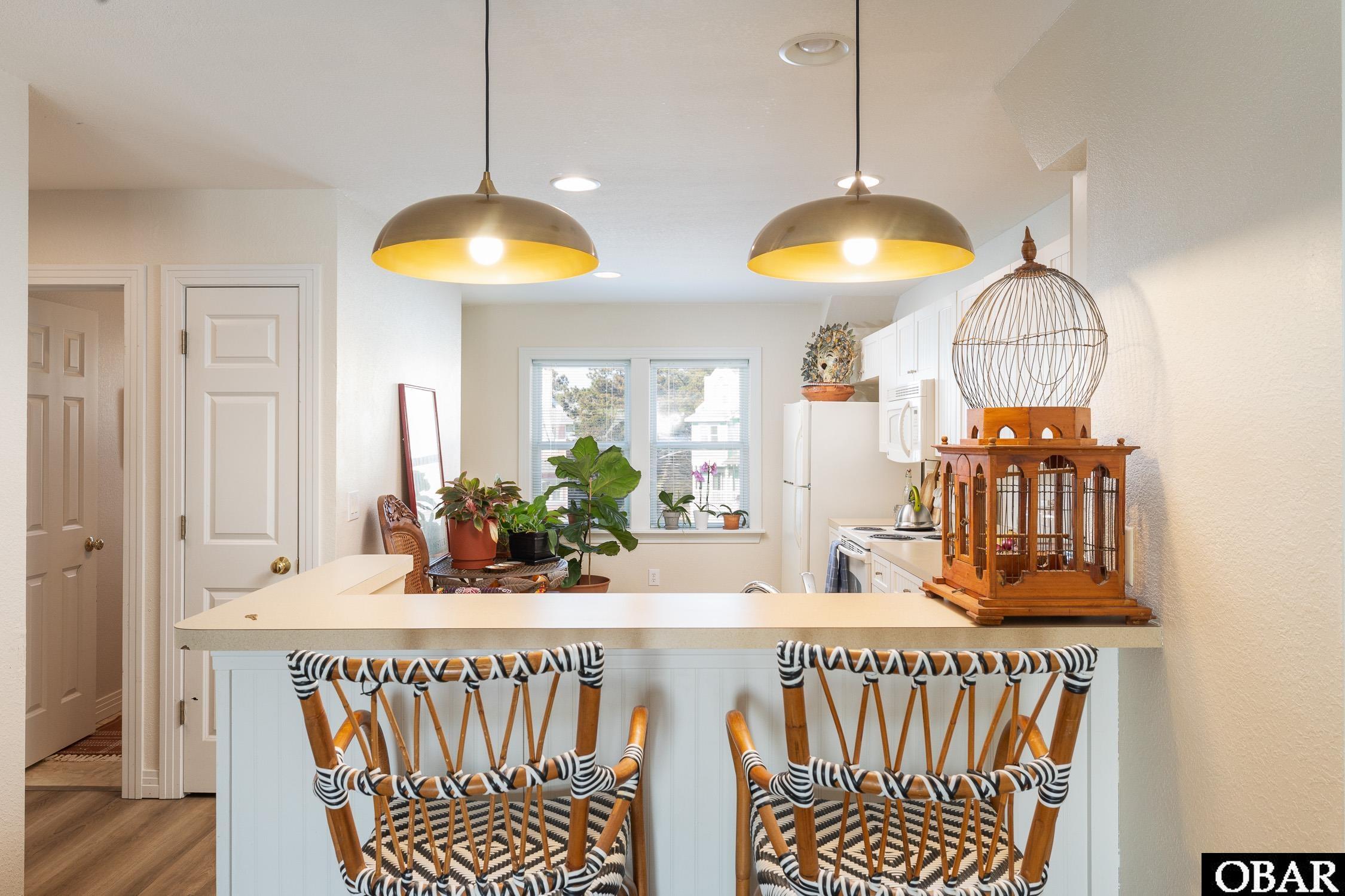 Kitchen with a breakfast bar, two woven stools, brass pendant lights, and white cabinets.