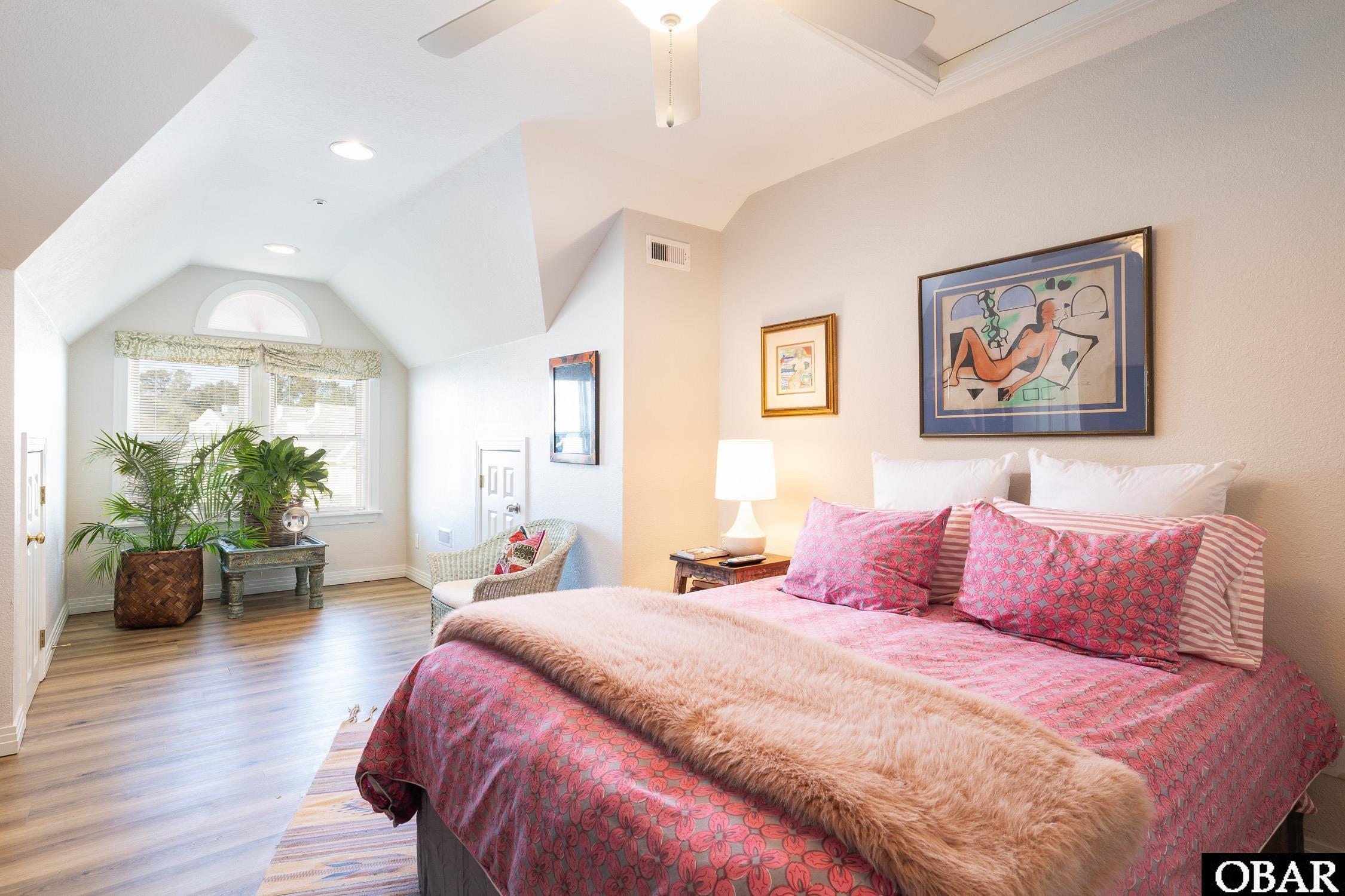 Furnished bedroom with a pink bedspread, sloped ceiling, and sunlit windows.