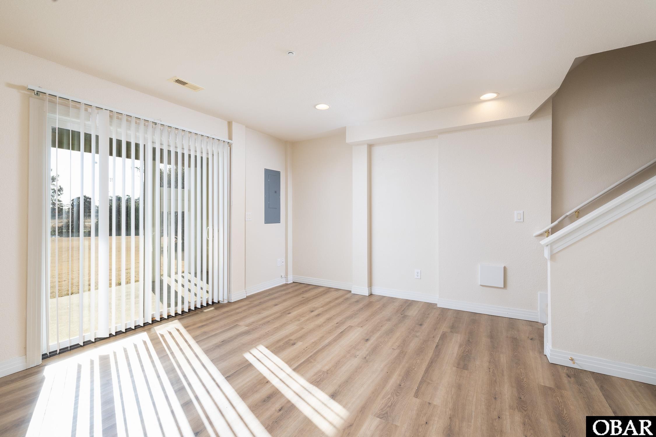 Vacant living area with wood-look flooring, vertical blinds, and a staircase.