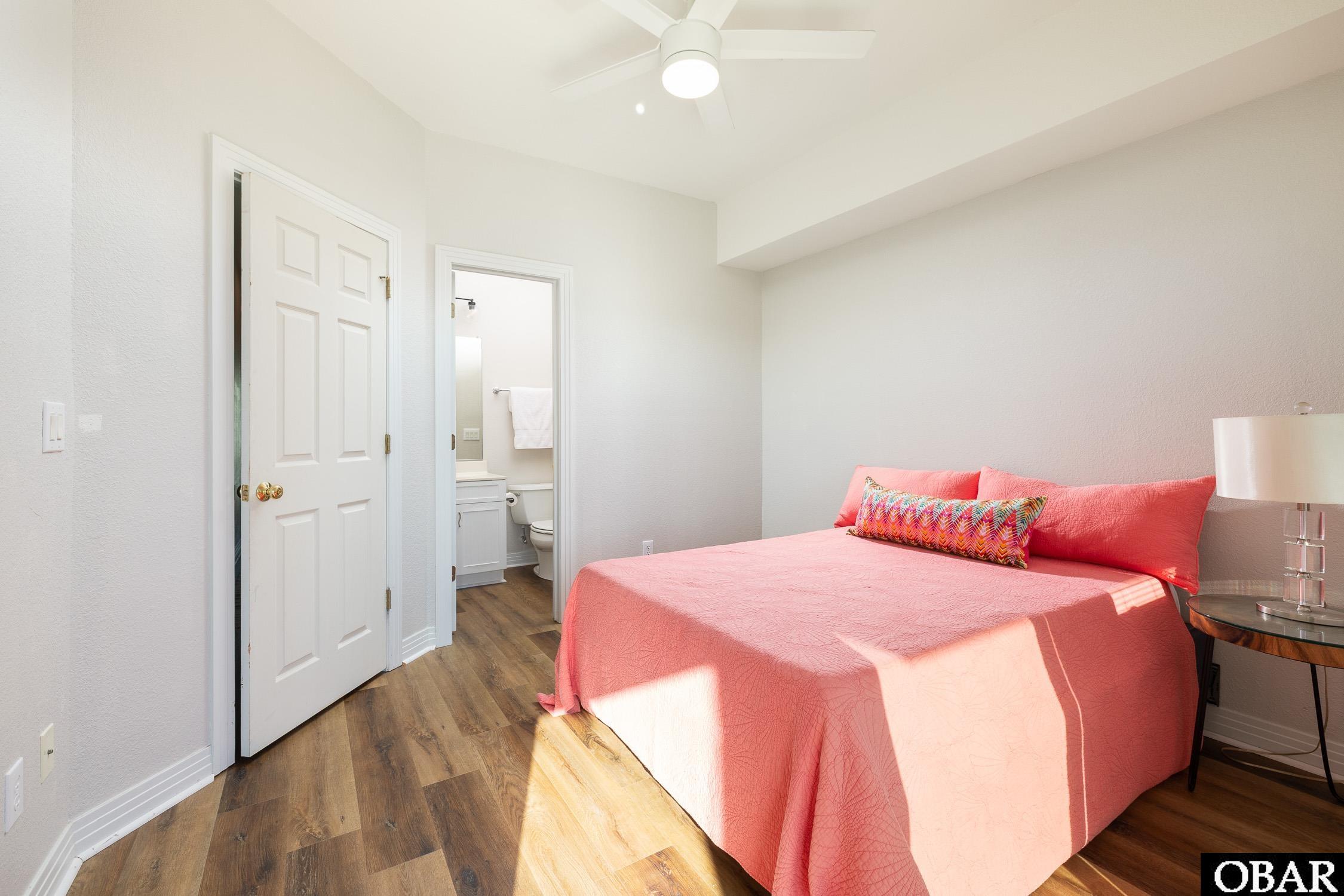 Bedroom with coral bedding, wood-look flooring, and an ensuite bathroom doorway.