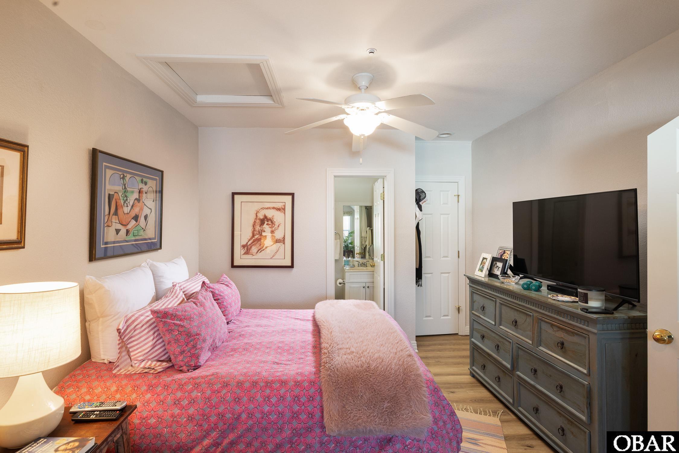 Bedroom with a pink patterned bedspread, ceiling fan, and television on a dresser.
