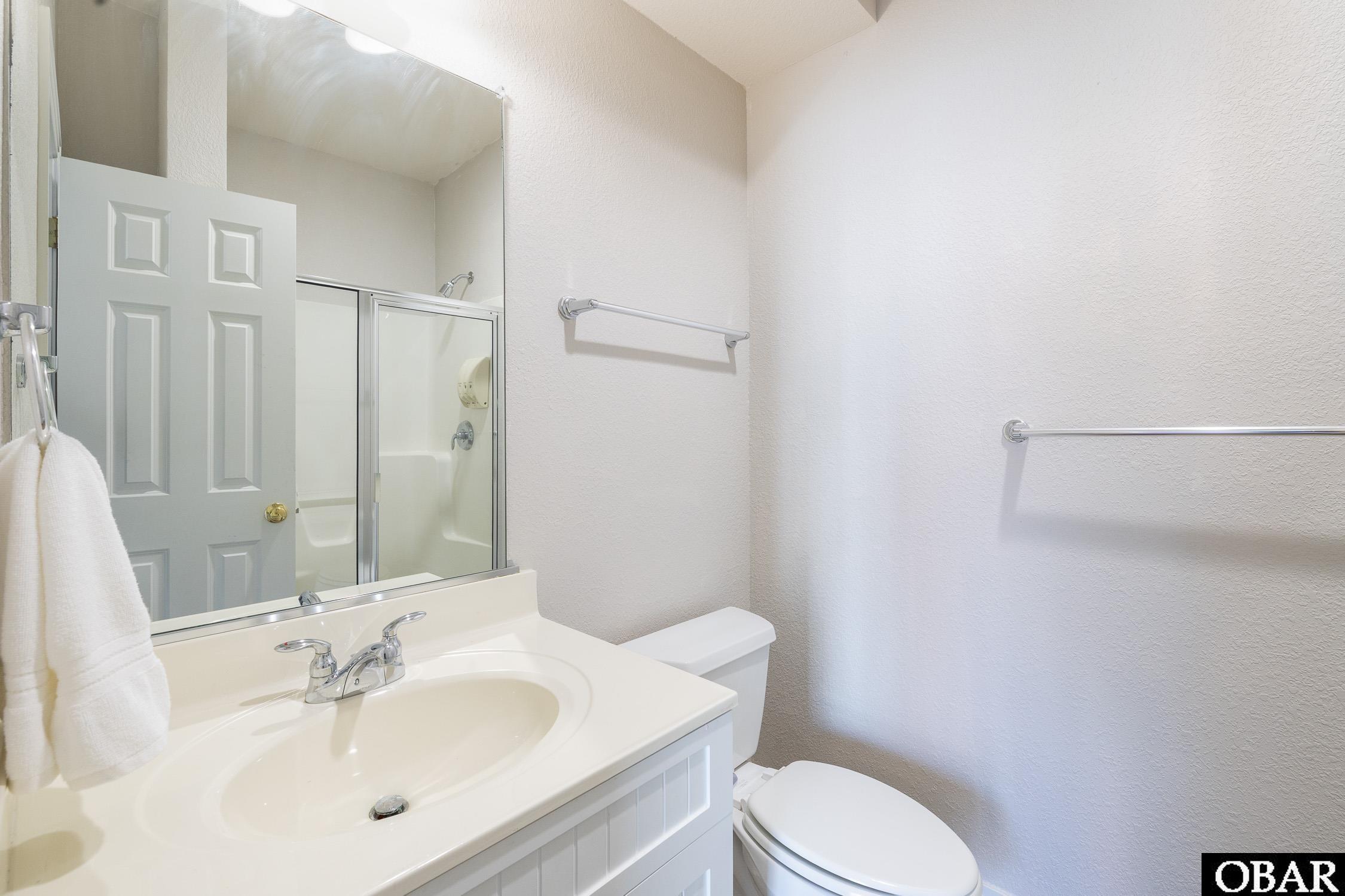 Bathroom with a white vanity and sink, toilet, and glass-enclosed shower reflected in the mirror.