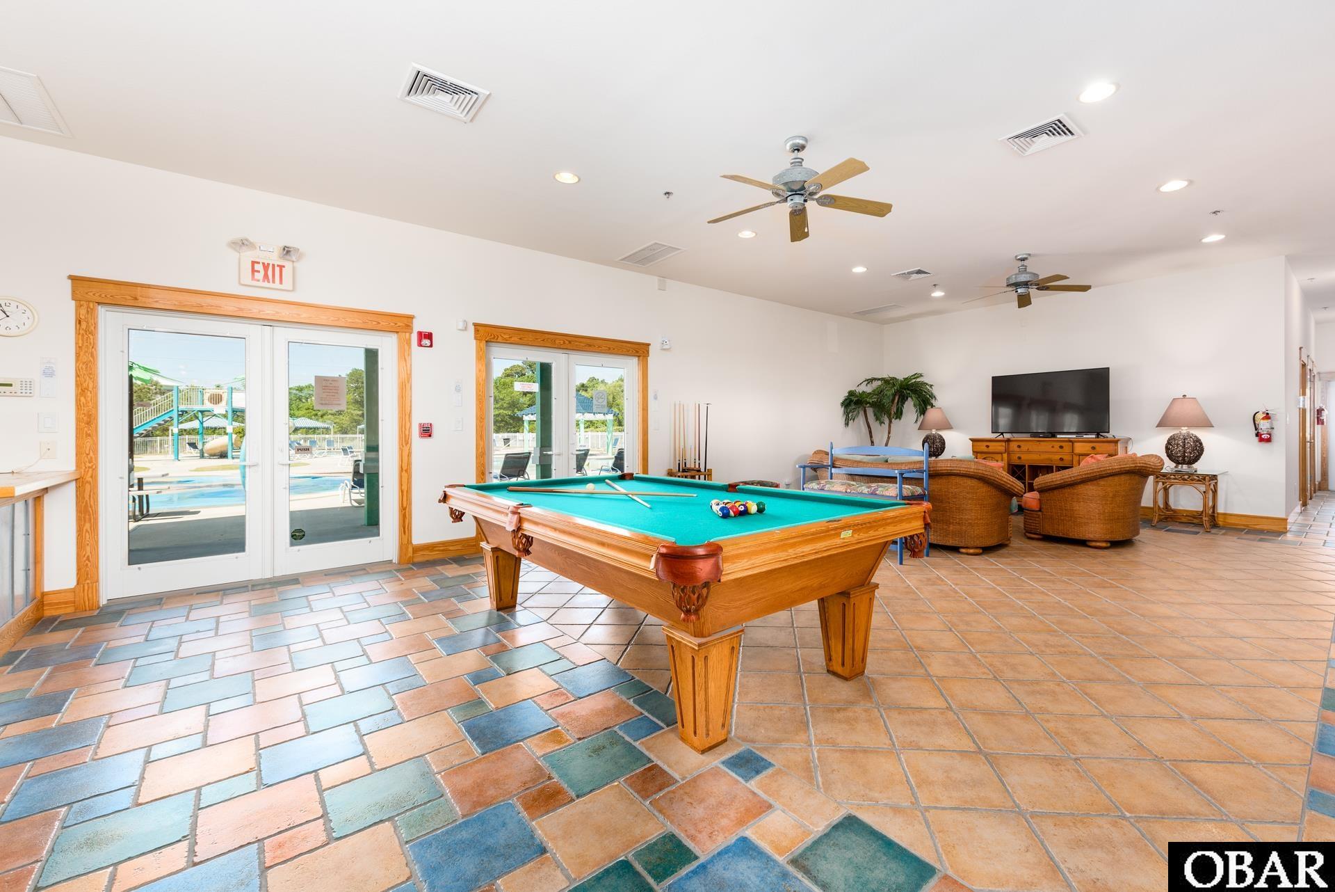 Community game room with a billiards table, lounge seating, and doors opening toward a pool.