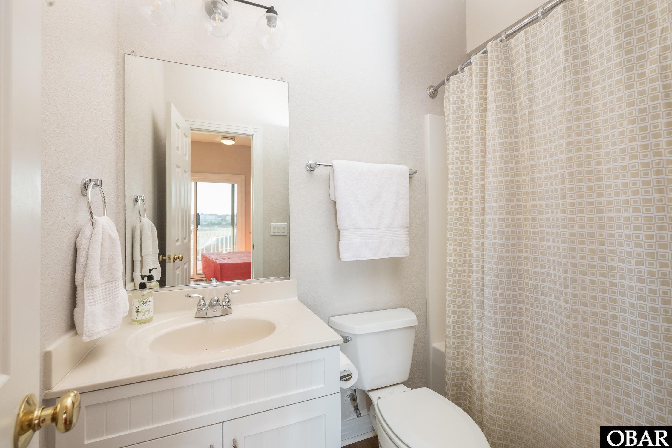 Bathroom with a white vanity, toilet, and beige geometric shower curtain.