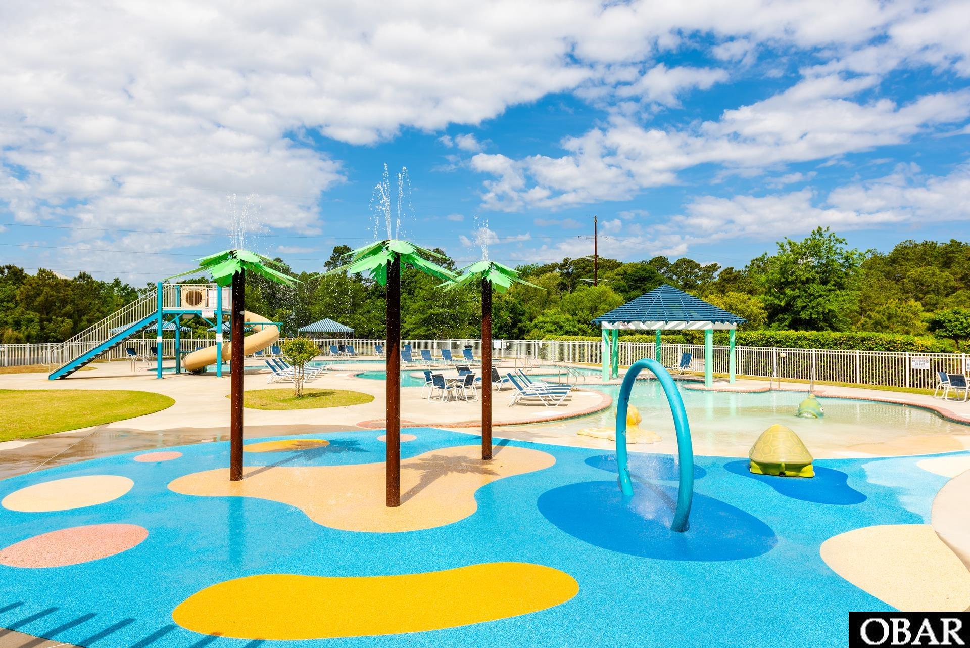 Community pool with a colorful splash pad, water features, and a children's slide.