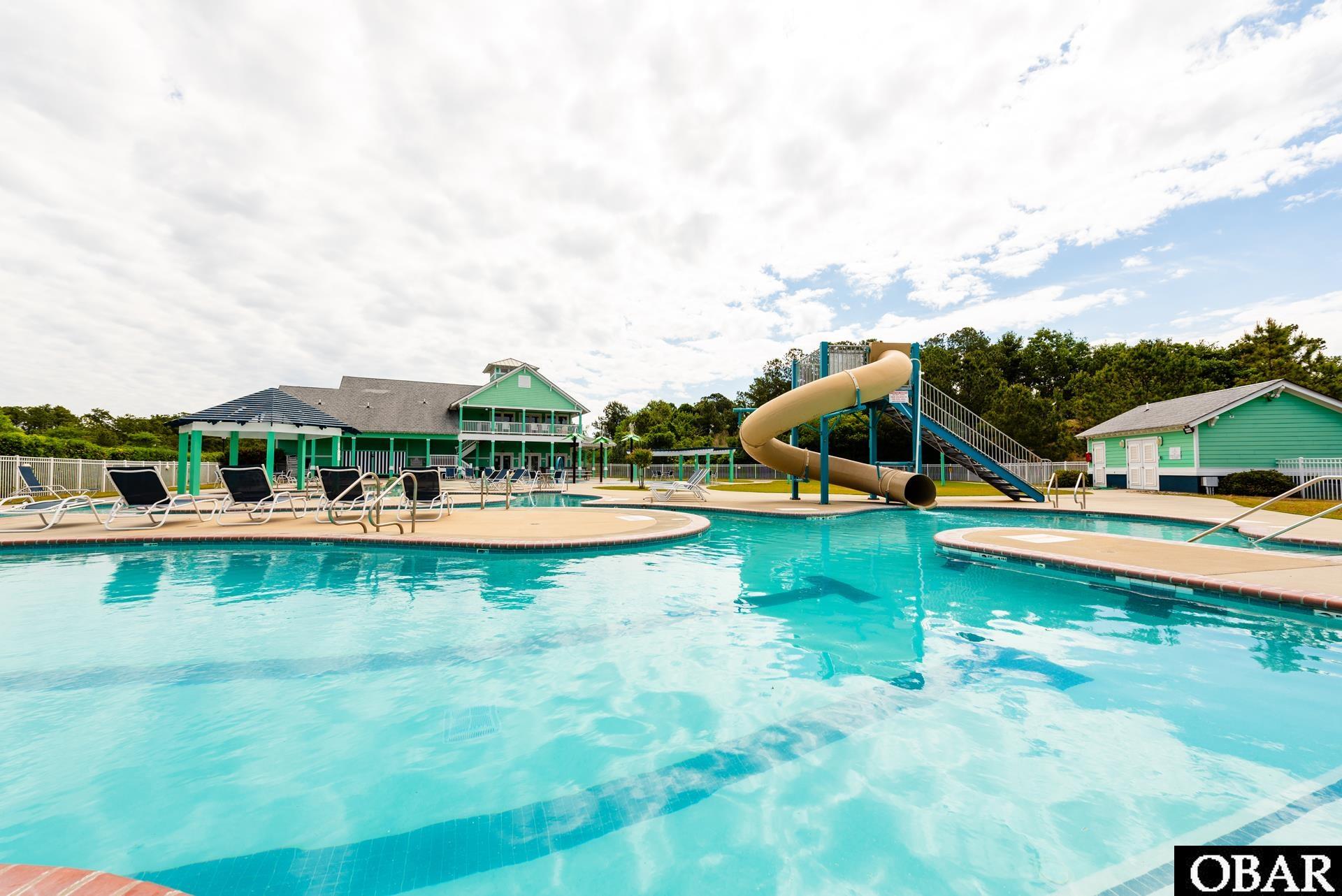 Community pool with a winding water slide, lounge chairs, and green clubhouse buildings.