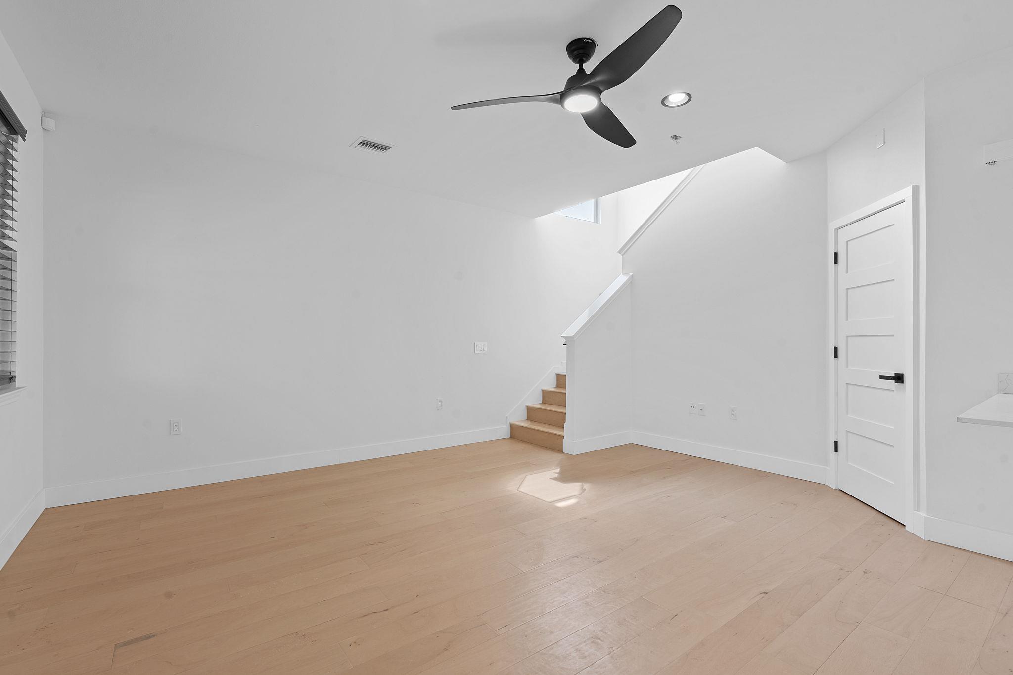 Unfurnished room with light wood floors, a black ceiling fan, and stairs leading upstairs.