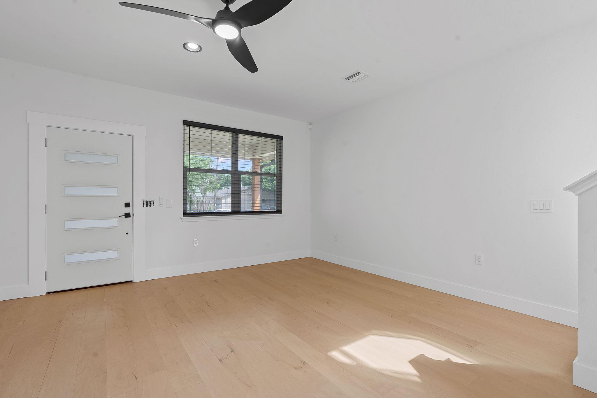 Vacant room with light wood floors, a modern front door, dark window blinds, and a ceiling fan.