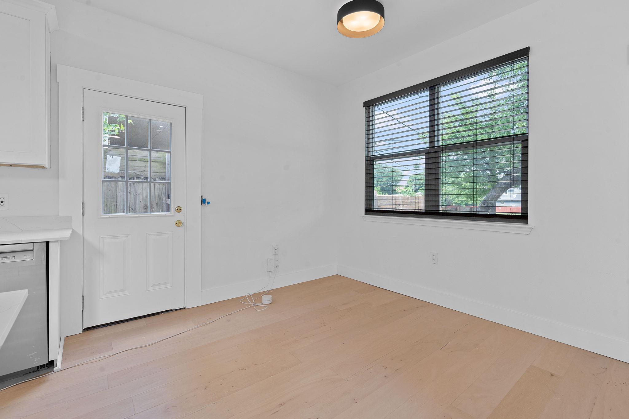 Vacant room with pale wood floors, a glass-paneled door, and a wide window with dark blinds.
