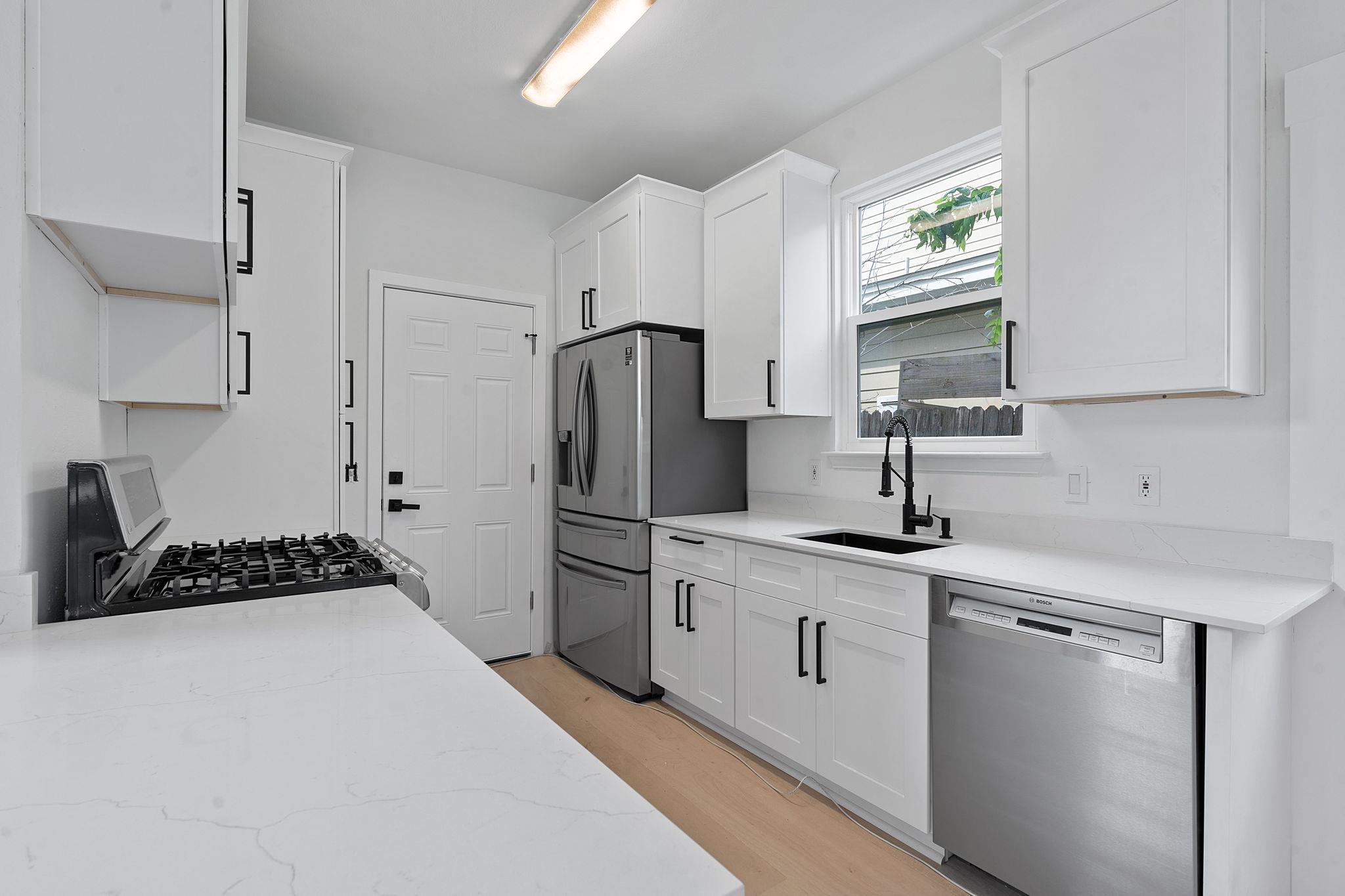 Modern white kitchen with veined countertops, stainless steel appliances, and a black gooseneck faucet.