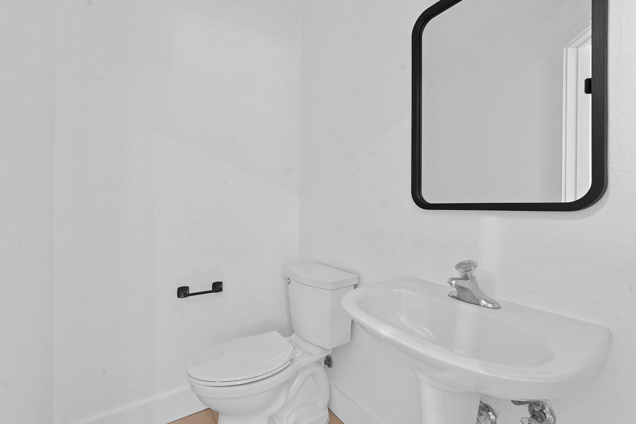 Bathroom with a white toilet, pedestal sink, and large black-framed mirror.