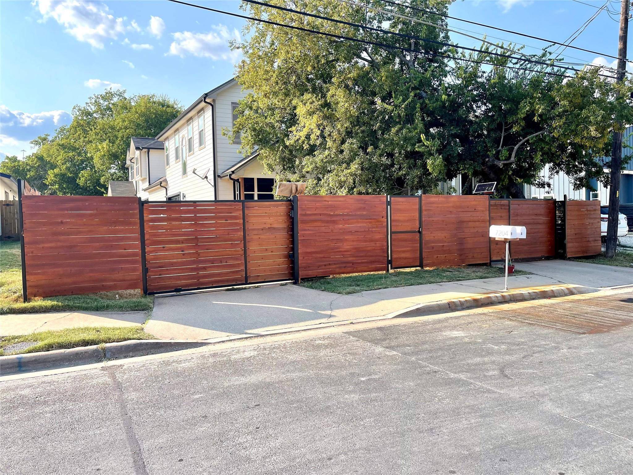 Two-story house behind a long reddish-brown wooden fence, with a driveway gate and mailbox marked 7204.