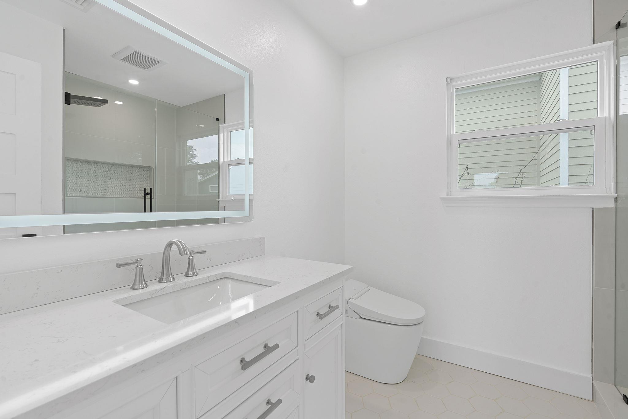 Bright bathroom with a long white vanity, large mirror, and glass shower with patterned tile.