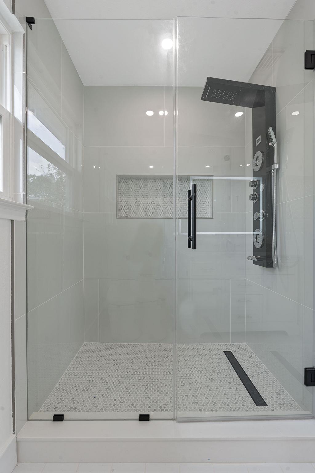 Glass-enclosed walk-in shower with gray tile, pebble floor, and rainfall showerhead.