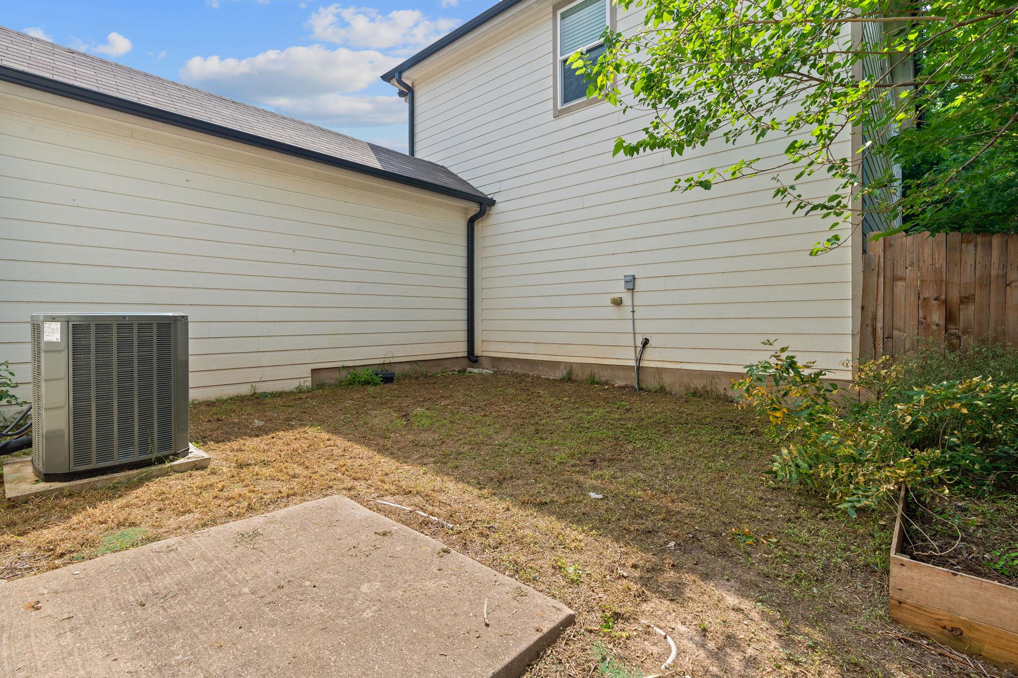 Small backyard with concrete patio, air-conditioning unit, wooden fence, and raised garden bed.