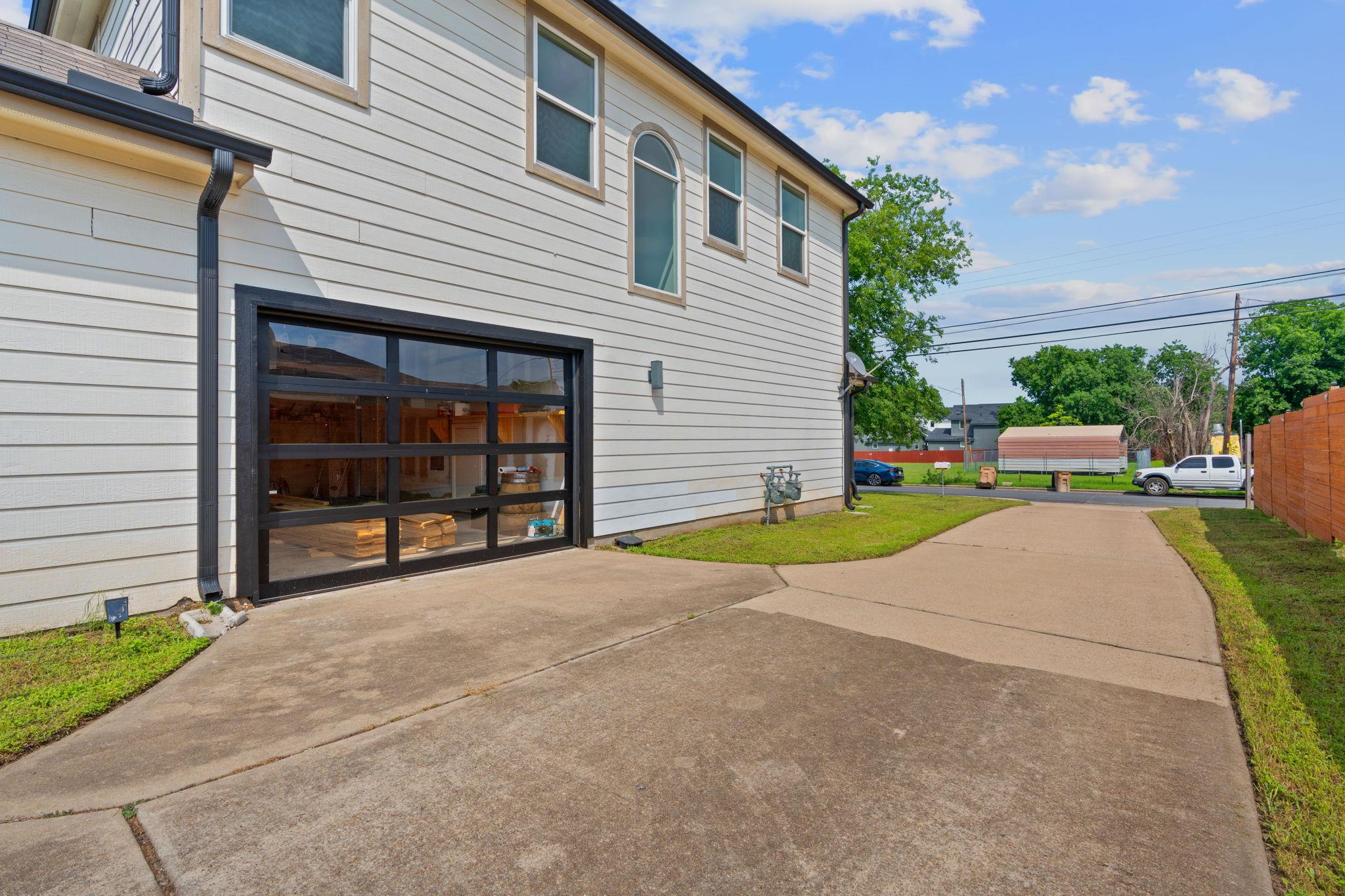 Home exterior with a black-framed glass garage door and broad concrete driveway.