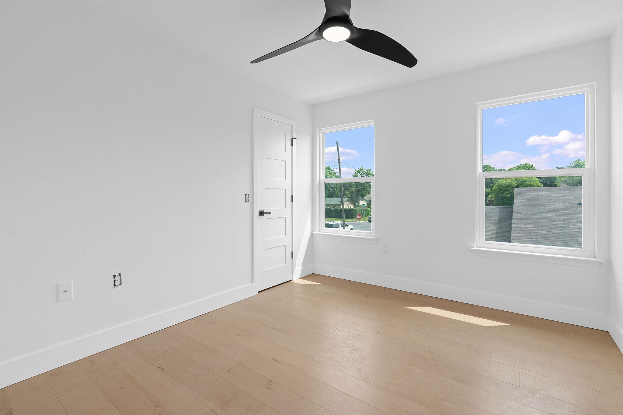 Vacant room with pale wood floors, two windows, and a black ceiling fan.