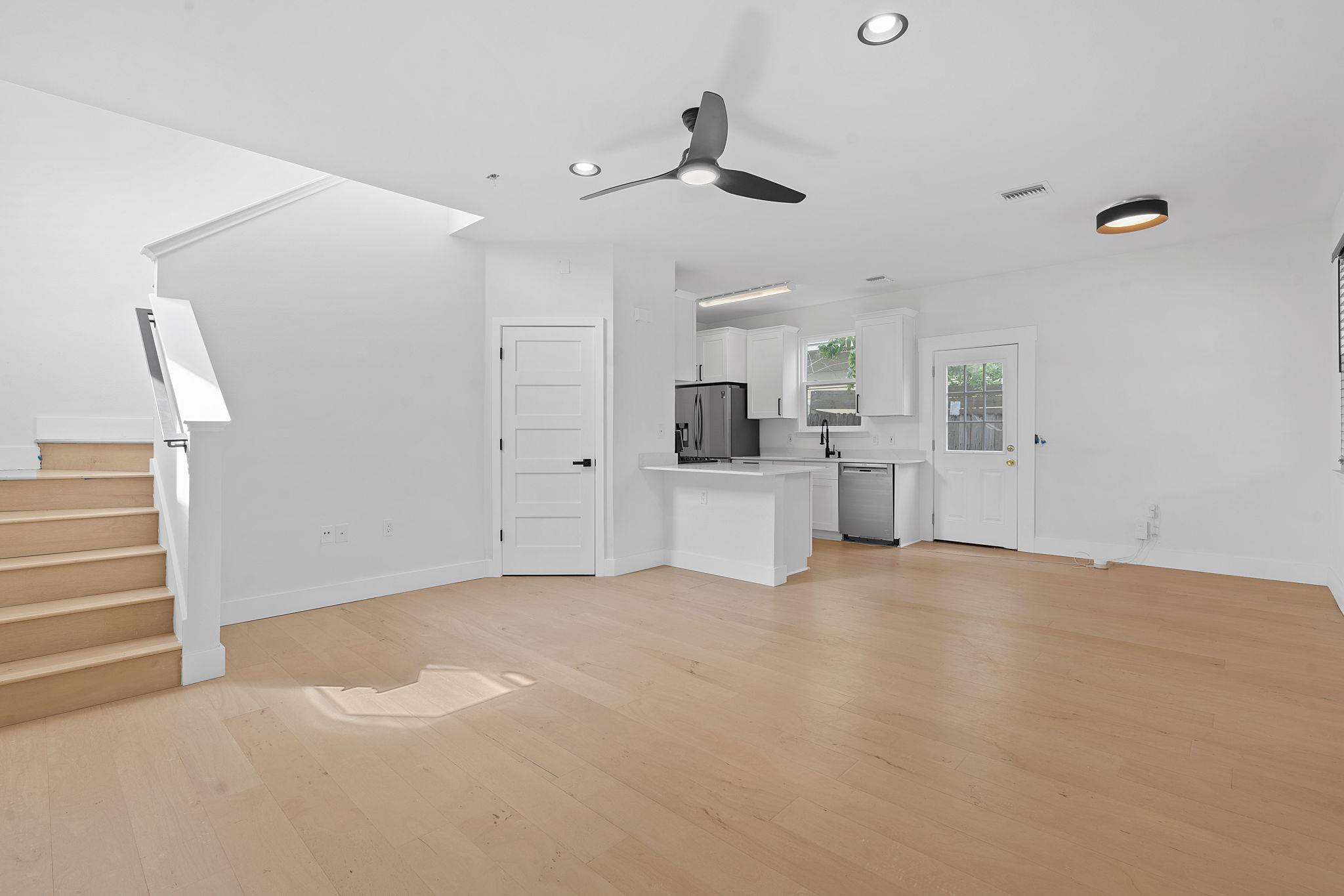 Vacant living area with a staircase, wood floors, and an open white kitchen.