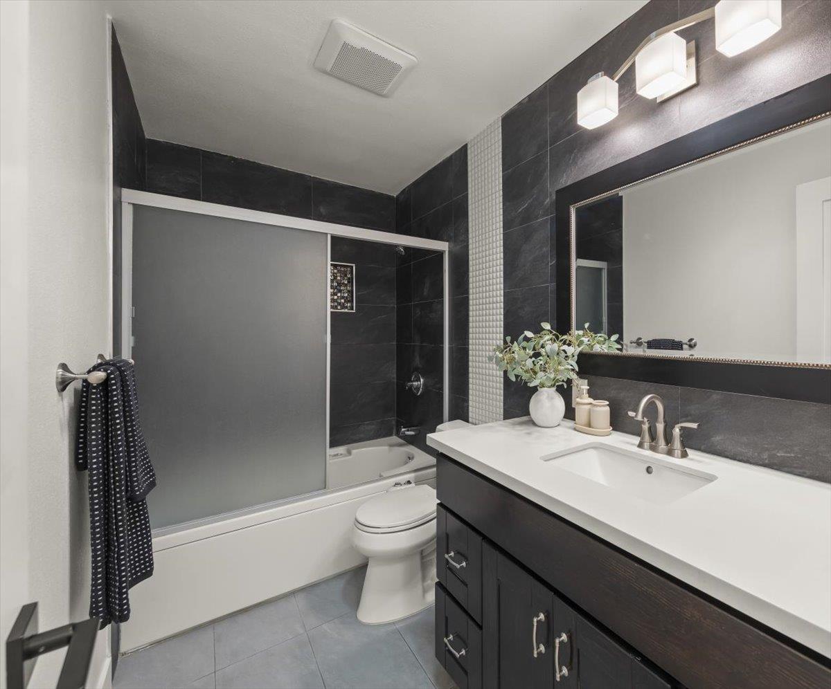 Bathroom with dark tile, frosted tub doors, and a white sink countertop.