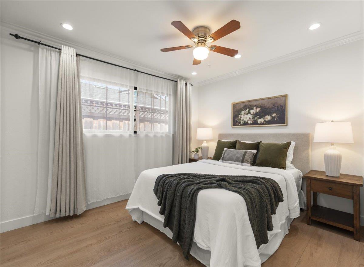Staged bedroom with a white bed, charcoal throw, and wood nightstand beneath floral wall art.