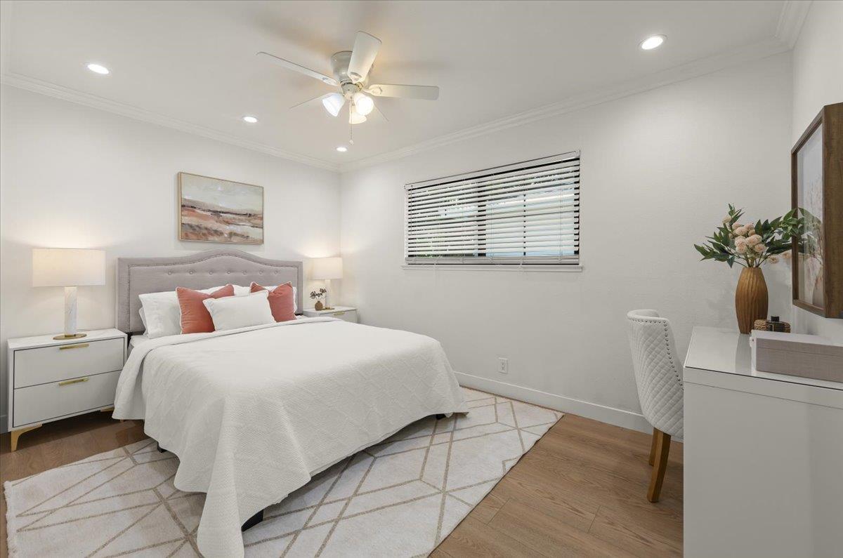 Staged bedroom with a gray upholstered bed, coral pillows, geometric rug, and desk by the window.
