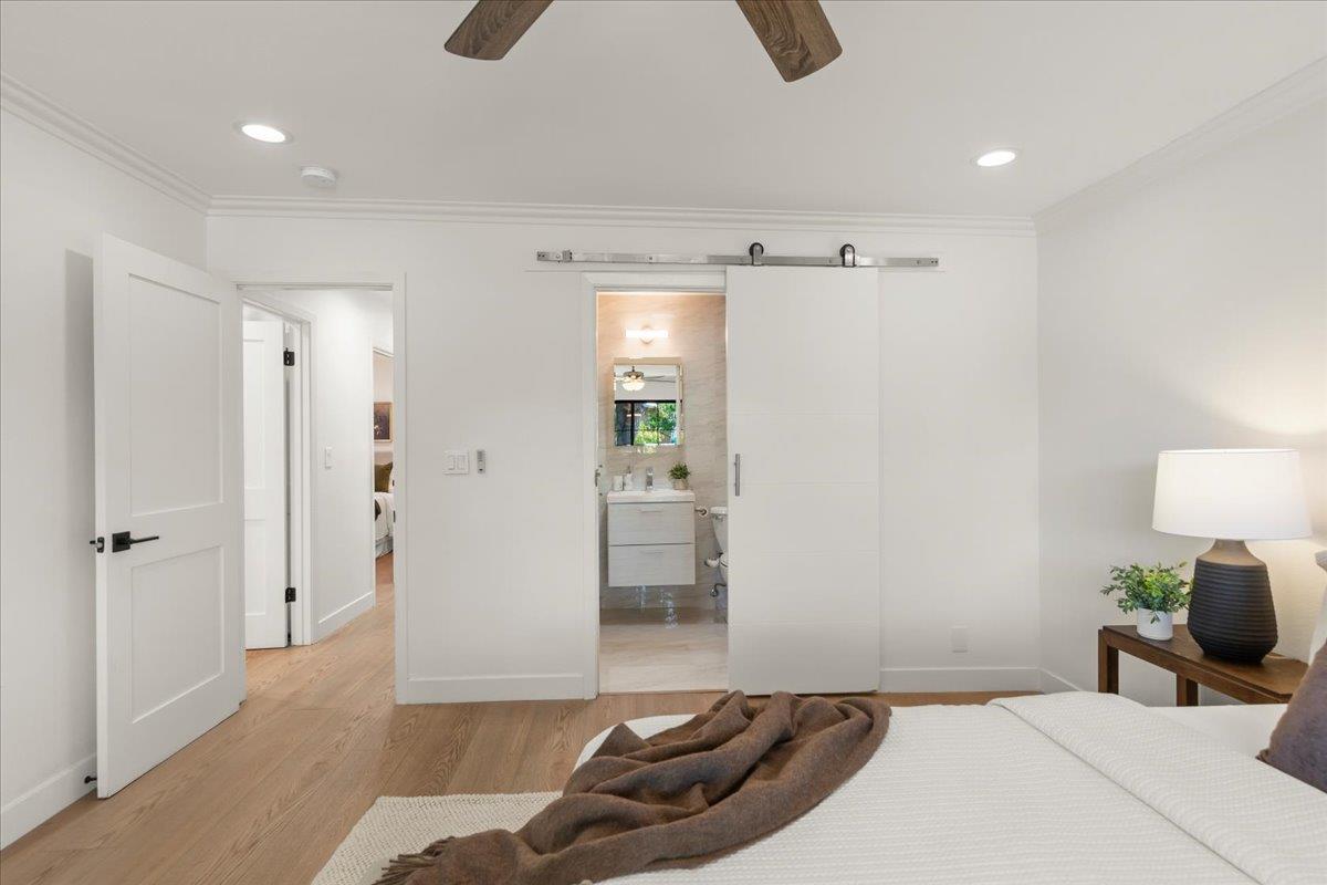 Staged bedroom with a white bed and sliding barn door opening to an ensuite bathroom.