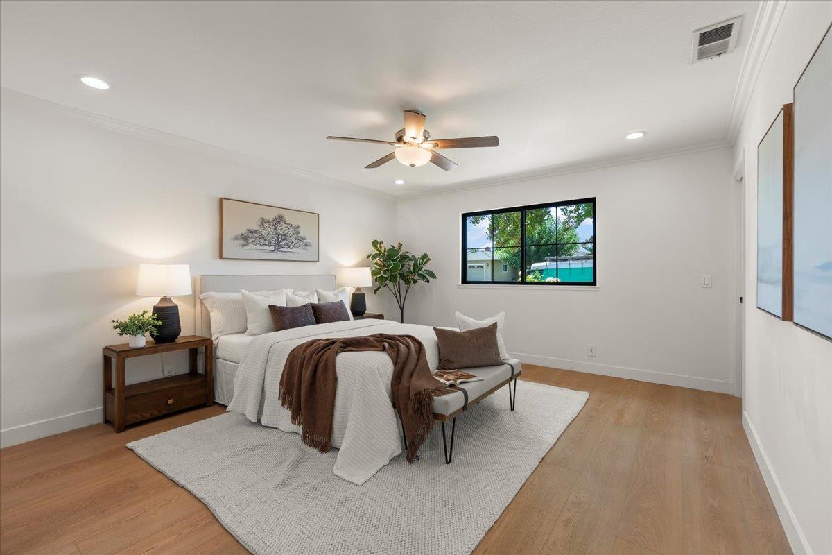 Staged bedroom with a white bed, brown accents, ceiling fan, and window overlooking a pool.