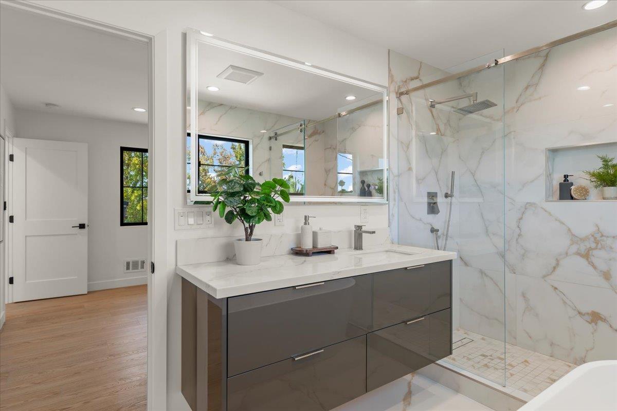 Renovated bathroom with a dark gray double vanity and glass shower lined with marble-look tile.