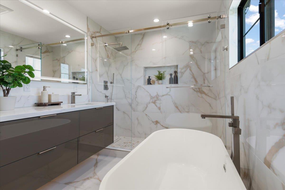 Modern bathroom with a freestanding tub, glass shower, marble-look tile, and dark vanity.