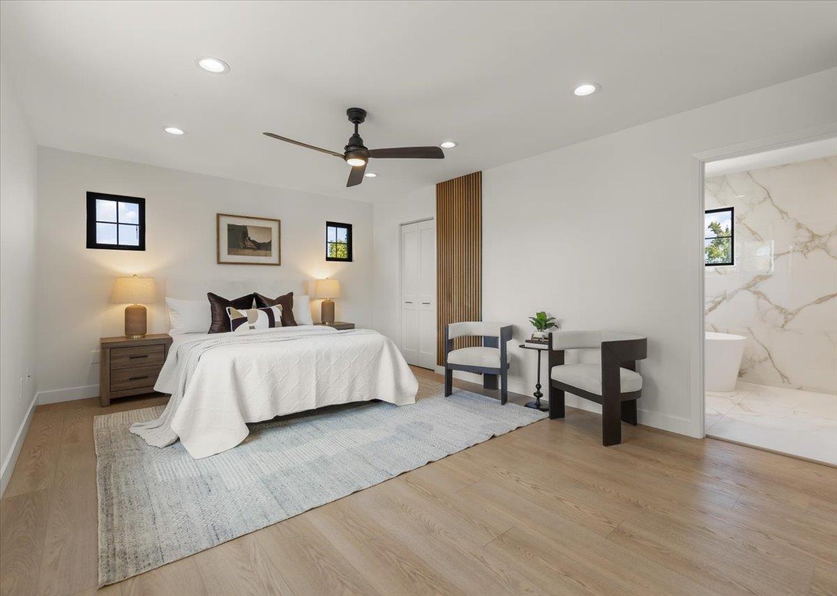 Staged bedroom with a white bed, pale rug, wood-slat accent panel, and doorway to a marble bathroom.