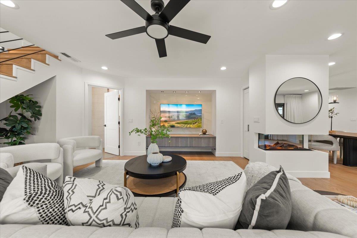 Staged living room with white sofas, a modern fireplace, round mirror, and staircase.
