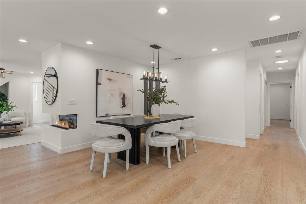 Open-plan dining area with a black table, upholstered chairs, chandelier, and fireplace.