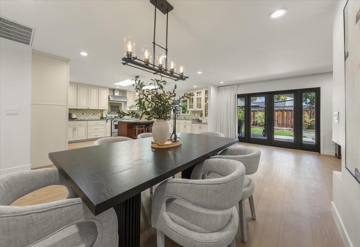 Open-plan dining room with a dark table, cream kitchen cabinetry, and black-framed doors to the backyard.