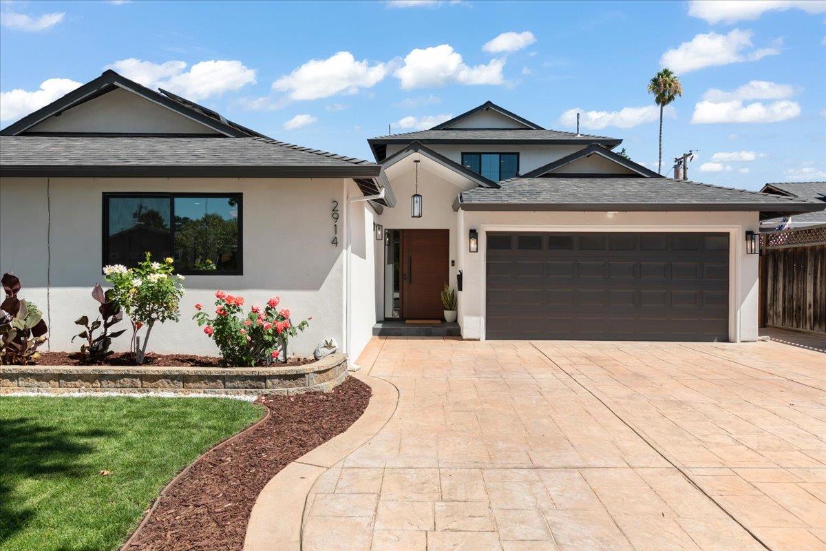 Home front with a wide paved driveway, attached double garage, and landscaped flower beds.