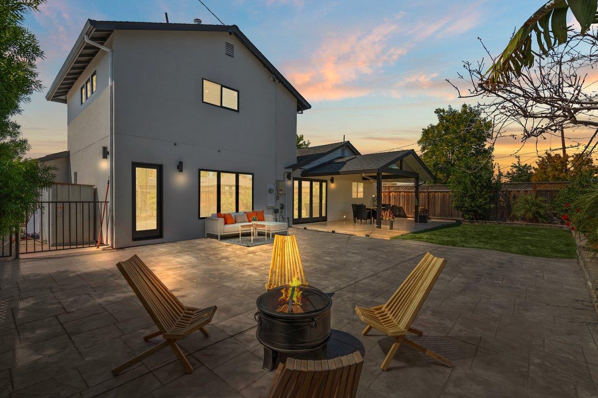 Modern two-story home behind a stone patio with a fire pit and covered seating at dusk.