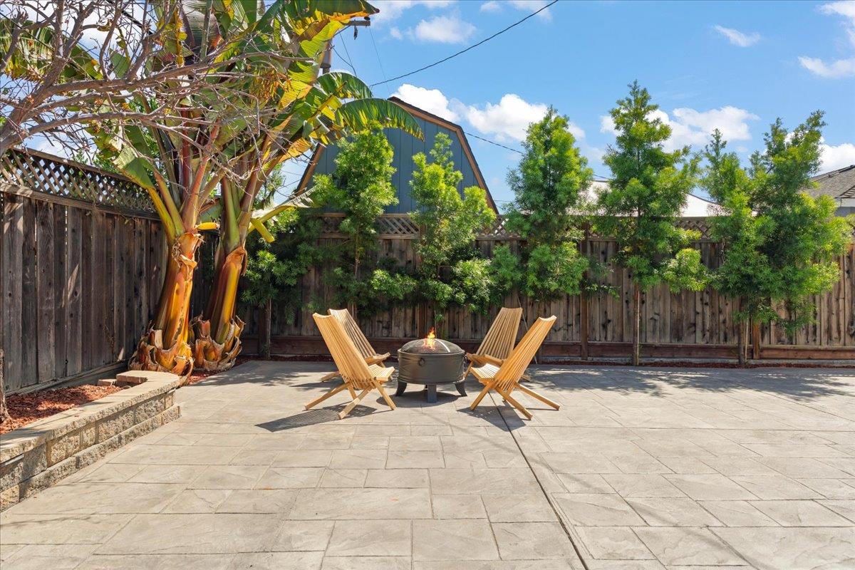 Backyard patio with lounge chairs around a fire pit, banana trees, and a wooden privacy fence.