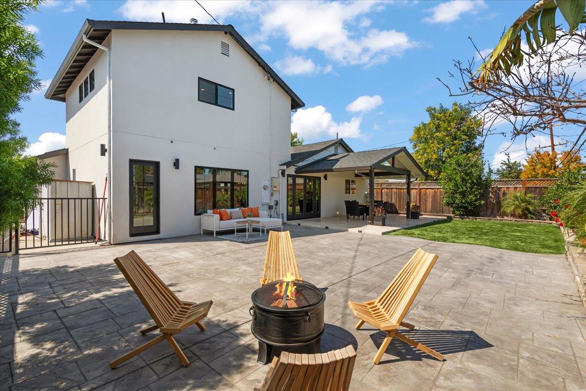 Modern two-story home with a paved backyard patio, fire pit, lounge chairs, and covered seating area.
