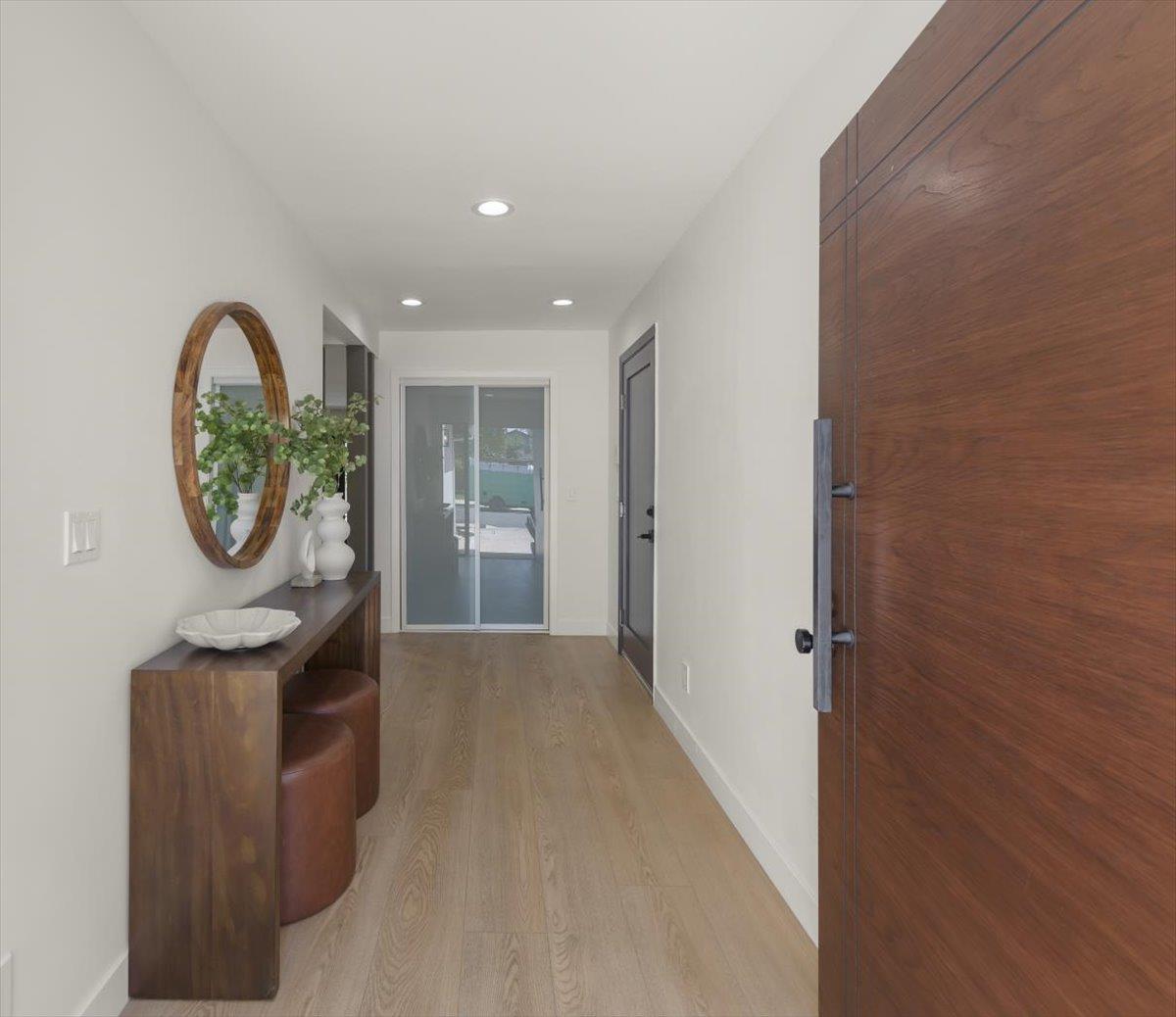 Entry hall with a wood console and oval mirror beside a large wood front door.