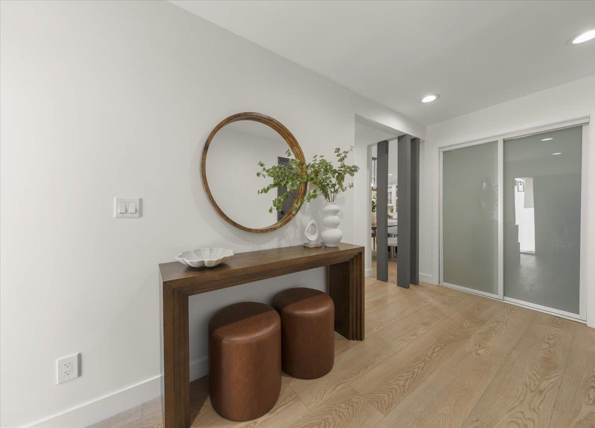 Modern entryway with a round mirror, dark wood console table, leather stools, and sliding glass door.
